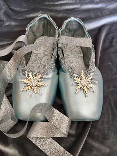 a pair of blue ballet shoes sitting on top of a black cloth covered floor next to silver ribbon