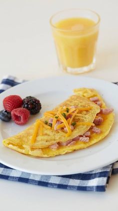 an omelet with ham, cheese and berries on a plate next to a glass of orange juice