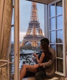 a woman sitting on a window sill looking out at the eiffel tower