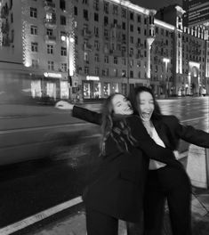 two women are posing for a photo in front of a cityscape at night