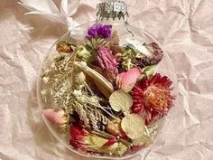 a glass ornament filled with dried flowers on top of a white table cloth