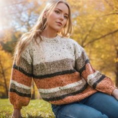 a woman sitting in the grass wearing a striped sweater