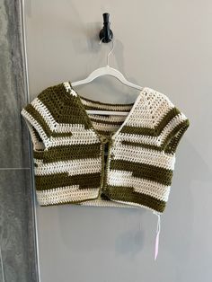 a green and white knitted sweater hanging on a wall next to a coat hanger