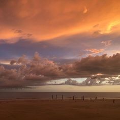 the sky is filled with clouds and people are walking on the beach