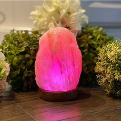 a pink himalayan salt lamp sitting on top of a wooden table next to some flowers