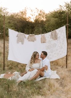 a man and woman are sitting on the ground with clothes hanging in front of them