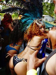 two women in bikinis and headdress are sitting on a boat, one is holding a bottle