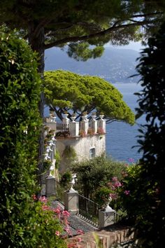 an old house is surrounded by greenery and flowers near the water's edge