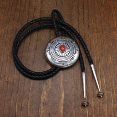 Sterling silver and coral bolo tie. The bolo is 2 3/8"diameter. The coral stone is 13 mm tall X 10 mm wide. It is sitting atop a floral look center.  There is a geometric ring around that. The outside edge has mountain and corn designs. The bolo is built like a round box. It is 7mm thick in the center. The cord and tips are 38" long. The bolo cord is 5mm thick. The inside is stamped C J Sterling. This piece is in good condition. Thank you for shopping in our store. Please let us know if you have Silver Lariat Bolo Tie With Adjustable Length, Silver Lariat Bolo Ties With Adjustable Length, Adjustable Sterling Silver Lariat Bolo Tie, Adjustable Sterling Silver Bolo Tie For Gifts, Silver Lariat Bolo Tie For Gift, Silver Bolo Tie With Sliding Knot As Gift, Formal Concho Bolo Ties, Elegant Concho Bolo Tie, Elegant Adjustable Concho Bolo Ties