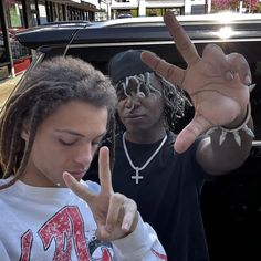 two young men standing in front of a car making the peace sign with their fingers