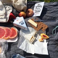 grapefruit, cheese, crackers, and fruit are on the picnic blanket