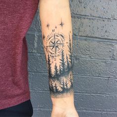 a man's arm with a compass and trees tattoo on the left side of his arm