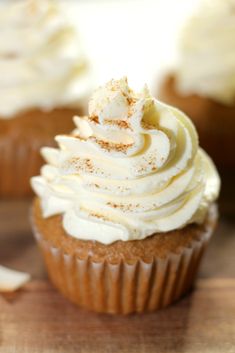 cupcakes with white frosting and cinnamon sprinkles on top are sitting on a cutting board