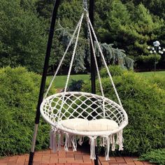 a white hanging chair with tassels in the middle of a brick patio area