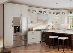 a large kitchen with white cabinets and wooden flooring, along with two bar stools