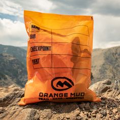 an orange bag sitting on top of a rocky hill with mountains in the back ground