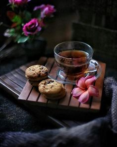 a cup of tea and some cookies on a wooden tray with flowers in the background