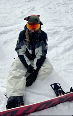 a person sitting in the snow with skis on their feet and wearing goggles