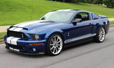 a blue and white mustang parked on the side of the road in front of some grass