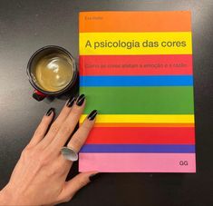 a woman's hand on top of a rainbow colored book next to a cup of coffee