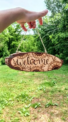 a hand holding a sign that says welcome hanging from a string in front of some grass