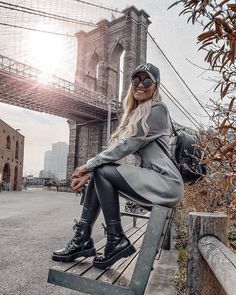 a woman sitting on top of a wooden bench next to a tall bridge in the city