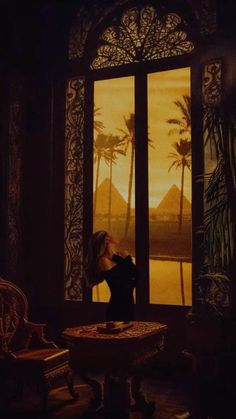 a woman standing in front of a window looking out at the desert and palm trees