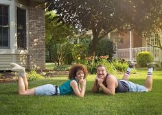 two people laying on the grass in front of a house talking on their cell phones