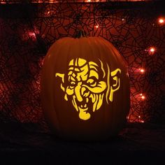 a carved pumpkin with an image of a demon on it's face is lit up in the dark