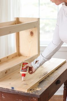 a woman sanding wood with a glue bottle on top of the wooden table in front of her