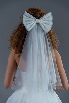 a woman wearing a white veil with a bow on it's head is looking at the back of her wedding dress