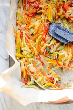 a pan filled with vegetables on top of a marble countertop next to a spatula