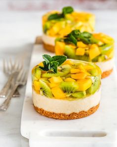 three small desserts with kiwi and mint leaves on white serving tray next to silverware