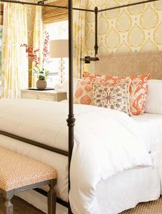 a bed with white sheets and pillows in a bedroom next to a window covered by yellow curtains