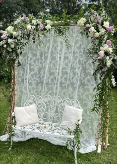 a white bench with flowers and greenery on it in front of a sheer curtain