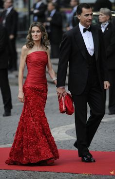 a man in a tuxedo and a woman in a red dress walking on a red carpet