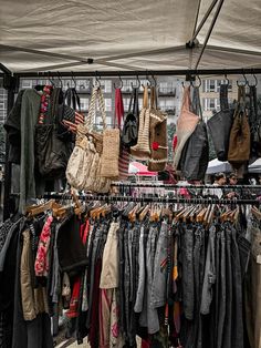 an outdoor market with clothes and handbags hanging on the rack in front of it