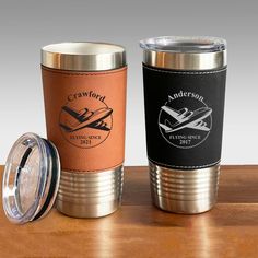 two travel mugs sitting on top of a wooden table