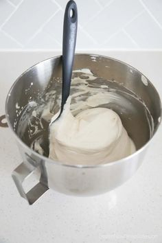 a metal bowl filled with cream sitting on top of a white counter next to a knife