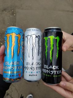 three cans of monster energy drink being held by two people's hands in front of the camera