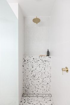 a white bathroom with black speckles on the floor and shower head in the corner