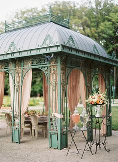 a green gazebo sitting in the middle of a lush green park with tables and chairs