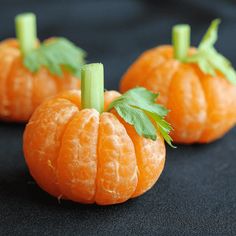 three small oranges with green leaves on them sitting on a black tablecloth covered surface