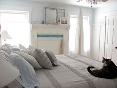 a black cat laying on top of a white bed in a bedroom next to a window