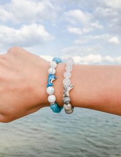 a woman's arm with two bracelets on it and the ocean in the background