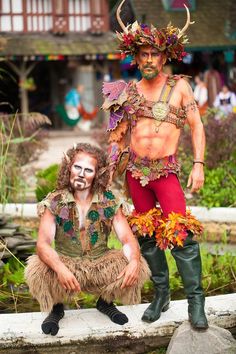 two men dressed up in costumes posing for a photo on a stone wall with plants and flowers around them