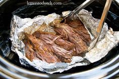 the meat is being cooked in the crock pot with tongs and paper wrapper