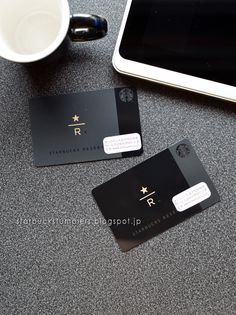 two black business cards sitting on top of a table next to a tablet and coffee cup