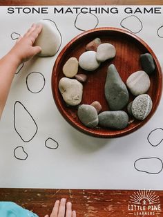 a child is playing with rocks in a wooden bowl on top of a paper sheet