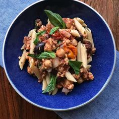 a blue bowl filled with pasta and vegetables on top of a wooden table next to a napkin